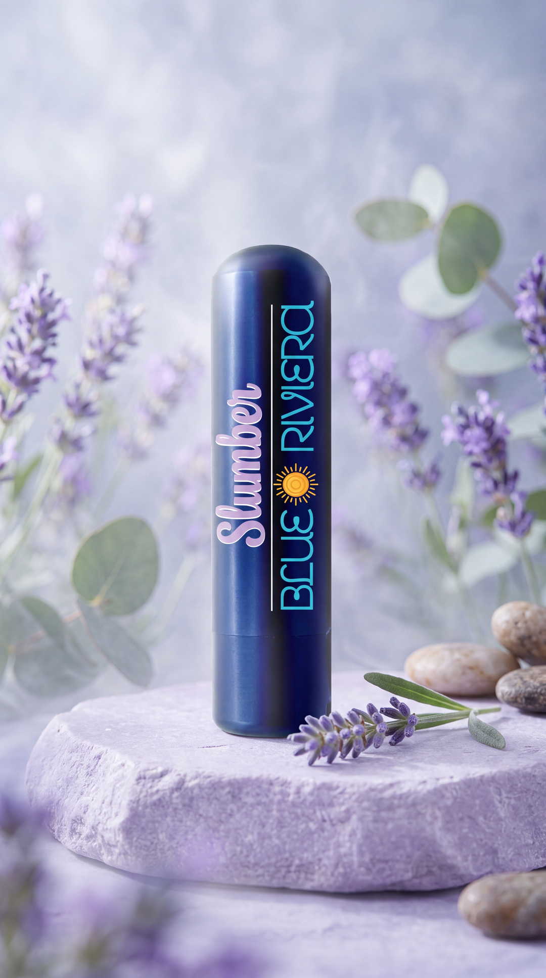 Blue Riviera Slumber aromatherapy inhaler on a pale purple stone surrounded by lavender sprigs, green leaves and smooth pebbles.